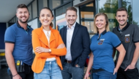 Un gruppo di collaboratori di ALDI Suisse è in piedi davanti a una filiale ALDI Suisse.