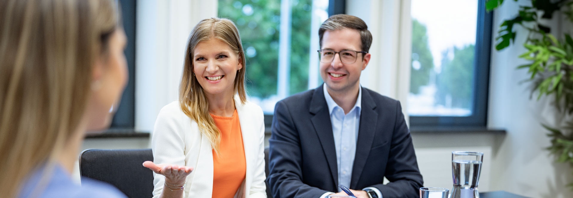 Une femme et un homme sont assis à une table et mènent un entretien d'embauche avec une autre femme. Les deux sourient.